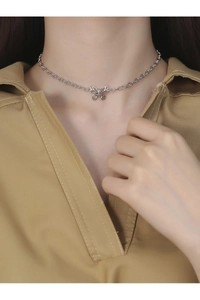 Gros plan d'un collier ras du cou papillon en argent porté par un mannequin au style épuré