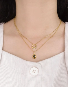 Détail du collier double rang doré avec pendentif rond et breloque en pierre noire