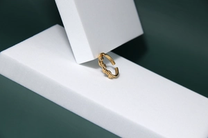 Détail d'une bague à nœud doré sur des blocs géométriques avec fond vert profond