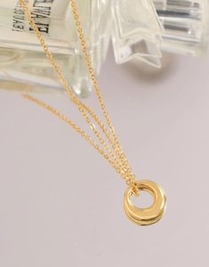 Gros plan du collier avec pendentif anneau doré minimaliste et chaîne croisée polie