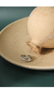 Close-up of a multi-layer silver winding ring on a textured ceramic plate