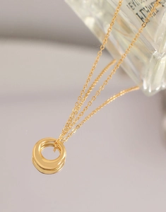 Gros plan d'un collier doré à double anneau en spirale avec reflet miroir et chaîne fine