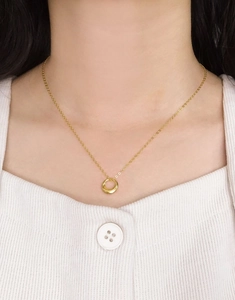 Gros plan d'un collier pendentif anneau doré minimaliste porté sur un pull en maille blanc