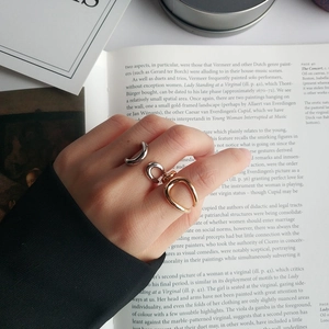 Close-up of three minimalist gold and silver U-shaped open rings worn on a hand over a book