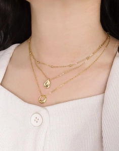 Gros plan de colliers dorés à trois rangs avec pendentifs perle, goutte et anneau