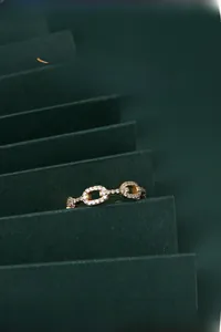 Détail macro d'une bague chaîne dorée avec micro-pavé de zircons sur fond vert foncé