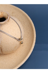 Close-up of minimalist silver chain featuring a polished gold spherical pendant on ceramic