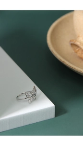 Detailed close-up of a silver hollow butterfly ring on a white geometric stand