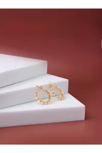 Macro detail of gold C-shaped hoop earrings featuring inlaid delicate white pearls