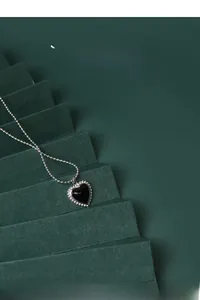 Detailed view of a black heart necklace with silver beaded edge on a green display