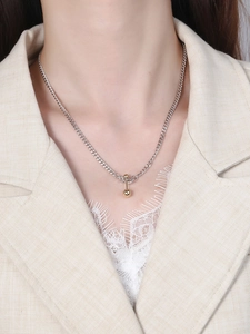 Detail of S925 silver Cuban chain with gold dumbbell pendant on a beige linen blazer