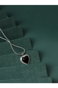 Detailed close-up of a silver heart necklace featuring a black onyx inlay on a green stand