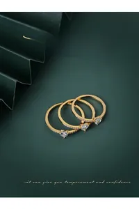 Dettaglio di tre anelli placcati oro con zirconi a cuore su sfondo verde scuro