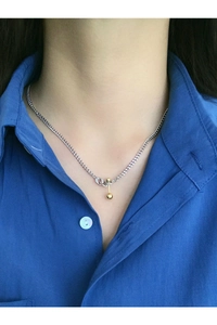 Detail of a minimalist silver curb chain with a gold bar and sphere pendant on a neck