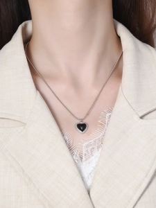 Detail of a black heart pendant necklace with silver beaded chain on a model