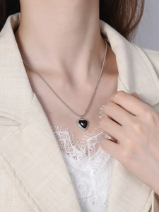Detail of a black heart pendant necklace with silver bead chain worn on a model