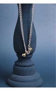 Detail of silver link chain necklace featuring a two-tone gold dumbbell pendant on stand