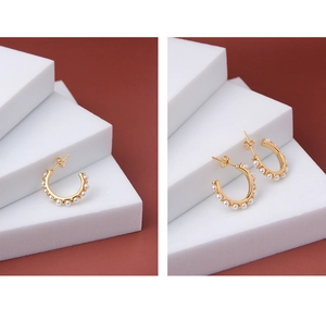Close-up of golden C-shaped hoop earrings with white pearls on a white geometric stand