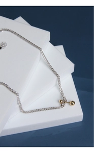 Close-up of minimalist silver chain with gold bead pendant on blue and white background