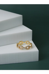 Détail macro d'une bague chaîne dorée ornée de zircons brillants sur fond vert foncé