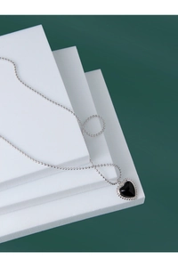 Macro view of black heart pendant with silver beaded chain on geometric white blocks