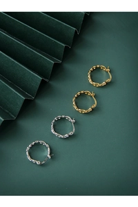 Macro detail of gold and silver pig nose link hoop earrings on a dark green background
