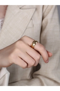Close-up of a wide golden ring with quilted pattern on a model hand with chic attire