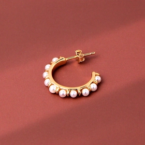 Elegant gold C-shaped hoop earrings with small white pearls on a warm red background