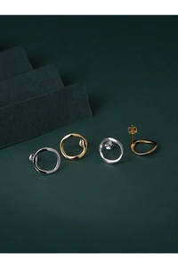 Macro detail of irregular wave-shaped silver and gold stud earrings on green background