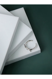Dettaglio di un anello a nodo d'argento su blocchi geometrici con sfondo verde scuro
