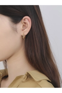 Close-up of a gold pig nose style earring on model ear showing metallic texture