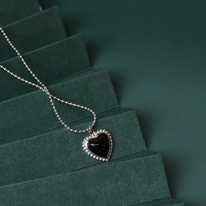 Minimalist black heart pendant necklace with silver beaded chain on green display