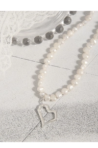Detail of freshwater pearl necklace with hollow silver heart pendant on lace background