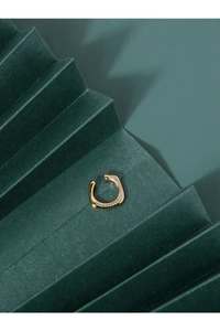 Détail d'une manchette d'oreille dorée sertie de zircons sur un fond créatif en papier vert