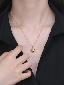 Dettaglio di una collana con ciondolo a cuore in oro lucido con catena a sfere sottile su modella