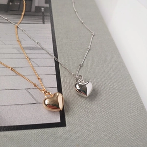 Dettaglio di pendenti a cuore lucidi in oro e argento con sottili catene a sfere
