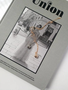 Dettaglio dei ciondoli a cuore in oro e argento su catenine sottili sopra una rivista