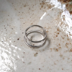 Macro detail of minimalist silver double-layer open ring on a ceramic textured surface