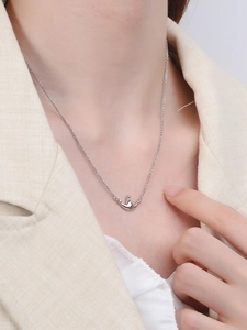 Close-up of polished silver crown pendant necklace on a model wearing a beige blazer