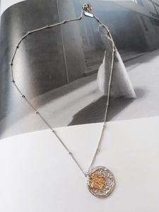 Détail du pendentif pièce bicolore argent et or avec texture lave sur une chaîne à perles fines