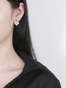Detail of silver heart earrings with angel relief worn by a model in a close-up view