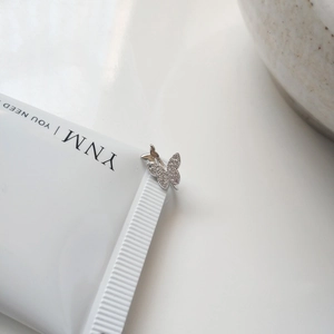 Detailed view of silver butterfly clip with zircon pavé setting on a minimalist background
