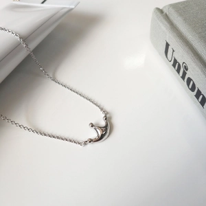 Minimalist crown pendant silver necklace shown on a grey fabric book with modern props