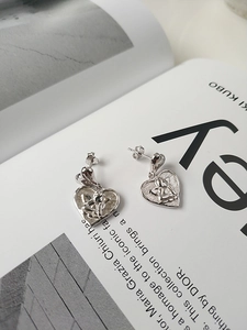 Detail of silver heart earrings with cupid angel relief on a minimalist white background
