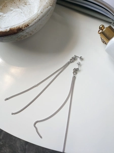 Detail of silver long tassel earrings with link chain on a marble surface