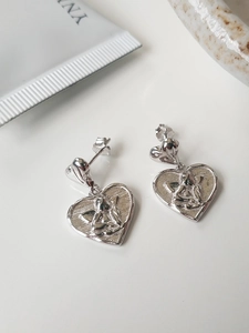Macro detail of silver heart earrings featuring embossed angel cherub on brushed metal