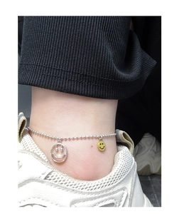 Détail d'une chevillère à perles argentées avec pendentifs smiley évidés et jaunes au pied