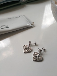 Detail of silver heart stud earrings with cherub relief on a minimalist white surface