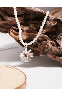 Close-up of pearl necklace with silver daisy pendant on natural wood display