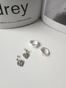 Detailed view of silver heart angel relief earrings and minimalist open rings on a desk